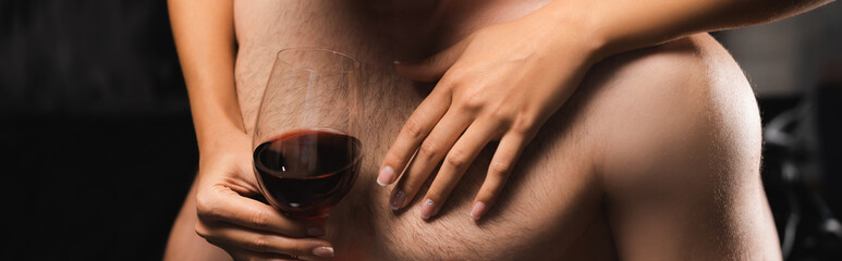 Fototapeta premium Cropped view of woman with glass of wine touching chest of shirtless boyfriend, banner