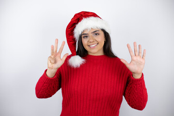 Young beautiful woman wearing a Santa hat over white background showing and pointing up with fingers number nine while smiling confident and happy
