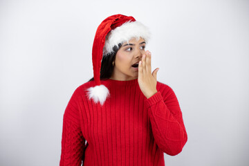 Young beautiful woman wearing a Santa hat over white background with her hand over her mouth and surprised, looking side