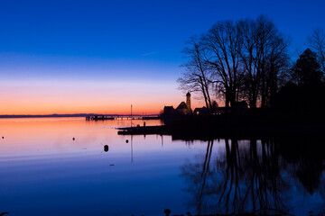 Sonnenuntergang am Bodensee mit Kirche im Hintergrund und Spiegelung vom Baum
