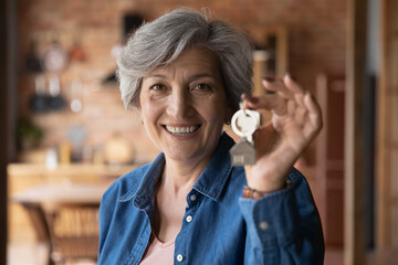 Head shot portrait smiling mature woman holding key from new home, own apartment, looking at...