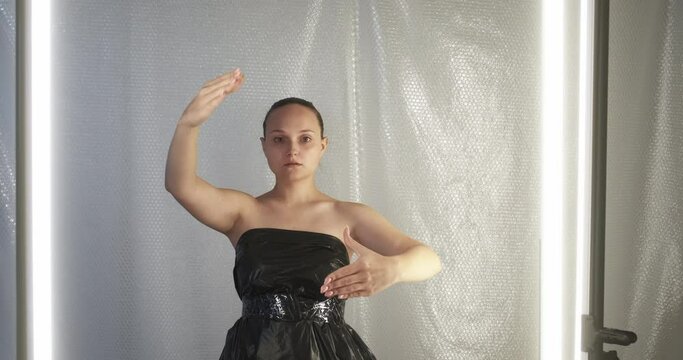 Mind control. Social manipulation. Propaganda brainwashing. Hypnotized marionette doll woman in black plastic bag dress waiting for instruction in isolation on bubble wrap background.