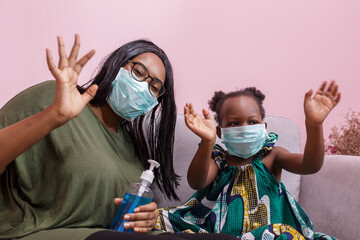 African Americans' mother and daughter wearing a mask are washing their hands with alcohol to...