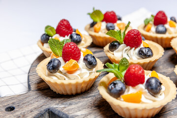 Fruit and berry tartlets dessert assorted on wooden tray. Closeup of delicious pastry sweets pies colorful cakes with fresh natural raspberry blueberry and cheese cream. French bakery catering.