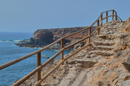 Beautiful views from the staircase of a lookout with a boat in the sea and the Cuevas de Ajuy in the background in Fuerteventura, Canary Islands, Spain