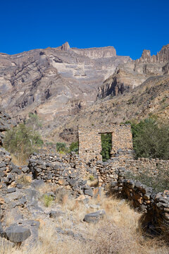 An abandoned stone house with two window openings stands amid the rugged mountains of Jebel Shams in Oman. The weathered structure and terraced landscape capture the timeless atmosphere of the Al Haja
