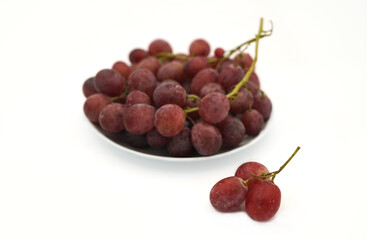 A plate of grapes and a small bunch of three grapes in front of the plate.