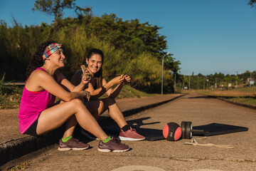 Two athlete friends eating cereal bars while resting - Young women runners with their cereal bars after training.