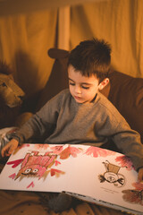 Little boy reading children's story in his teepee room.