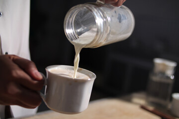 Making hot cream coffee, barista bar keeper pouring whipped milk cream into coffee cup