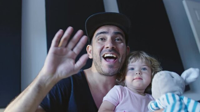 Man with daughter in lap waving to camera