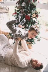 Close-up of young father lifting his son in his arms by the christmas tree