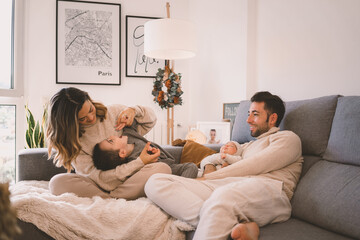 Young family with their little one and their baby enjoying and playing on the sofa at home during Christmas