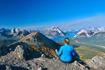 Naklejka premium Woman meditating on mountain top in front of beutiful lake and snowcapped peaks in Canadian Rockies. Alberta. Canada 