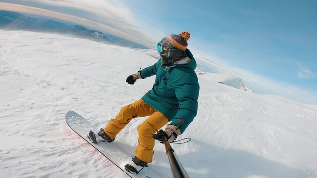 Guy filming himself during riding down. Man riding on snowboard with selfie stick in his hand downhill kamchatka mountain. Concept of extreme, sport, winter, freeride, snowboarding