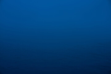 Natural texture of deep blue calm water in dusk close up. Night sea of blue classic color. Water ripple nature background. Meditative image of thick fog above lake. Soft light shines on water surface.