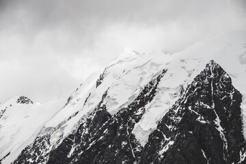 Atmospheric minimalist alpine landscape with massive hanging glacier on snowy mountain peak. Big balcony serac on glacial edge. Low clouds among snowbound mountains. Majestic scenery on high altitude.