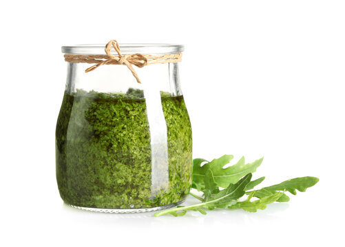 Jar of tasty pesto and arugula on white background