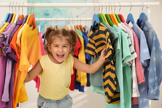 Funny little girl choosing clothes on rack indoors