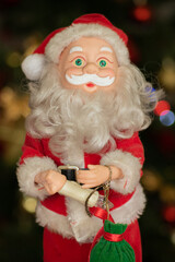 Santa Claus doll with candle in hand and small green gift bag and bokeh in the background