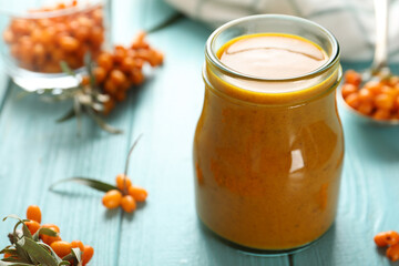 Delicious sea buckthorn jam and fresh berries on light blue wooden table. Space for text