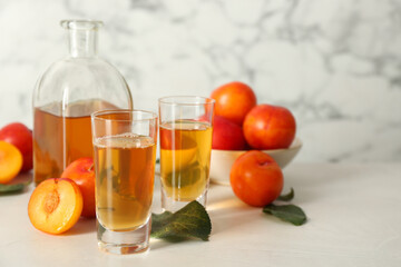 Delicious plum liquor and ripe fruits on white table. Homemade strong alcoholic beverage