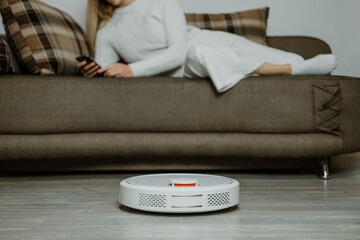 Robotic Vacuums, Robot Mops. Smart home. Robotic Vacuum Cleaner while Woman Relaxing on sofa....