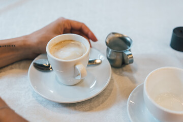 Small white cup of cappuccino stands on the table
