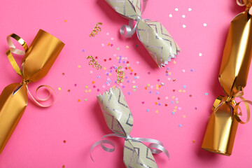 Open and closed Christmas crackers with shiny confetti on pink background, flat lay