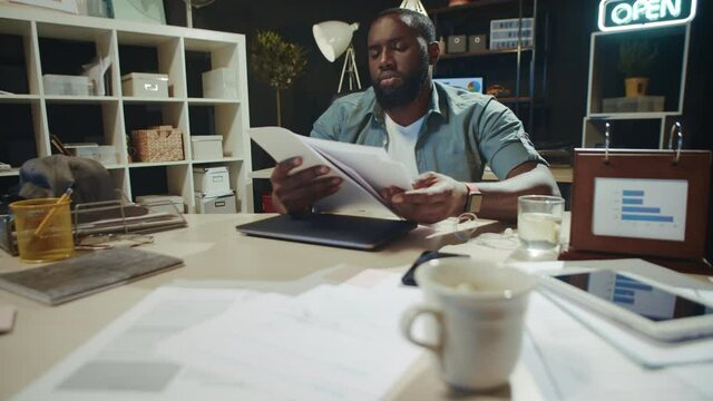 Focused african man reading documents in late office. Afro guy working overtime