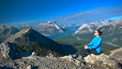 Naklejka na ściany i meble Middle age caucasian woman hiker on mountain top relaxing and enjoying view of lake and mountains in Canadian Rockies. Alberta. Canada