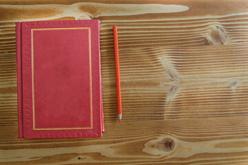 antique red gilded book on the old wood table with colorful pencils for distance learning, Closed old book on vintage wooden background. . Closed book with empty cover laying on wooden table