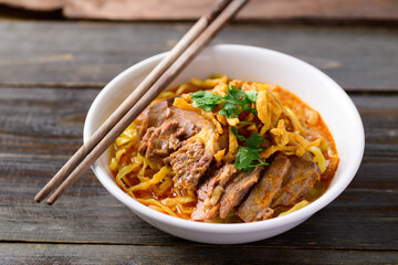 Northern Thai food (Khao Soi), Spicy curry noodles soup with beef in a bowl and chopsticks on wooden background