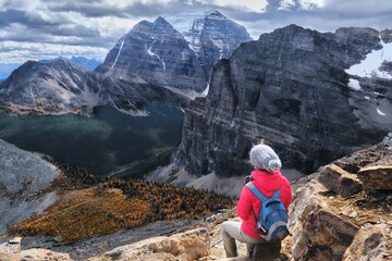 Woman hiker sitting on rock looking down on valley with yellow larch trees. Fairview mountain in Banff National Park. Alberta. Canada 