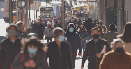 Anonymous crowd of people walking street wearing masks during covid 19 coronavirus pandemic