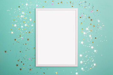 Festive mint background with blank white photo frame and scattered confetti. Mock up for photo or text. Top view. Flat lay style.