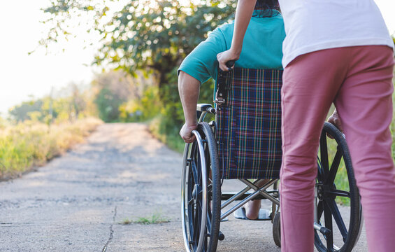 Rear view of disabled handicapped man in wheelchair and care helper walking in park.