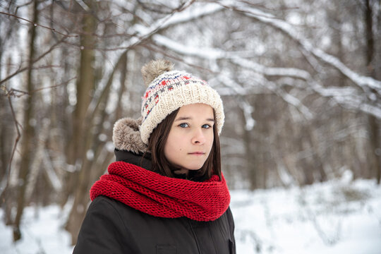 Portrait of a cute teen girl in a knitted cap and red scarf in the forest