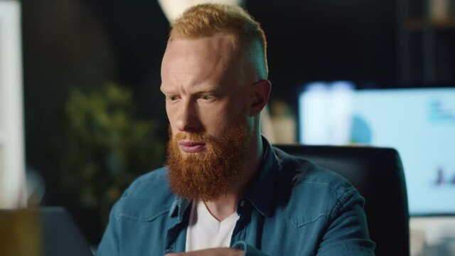Focused hipster man reading message on laptop computer in night office.