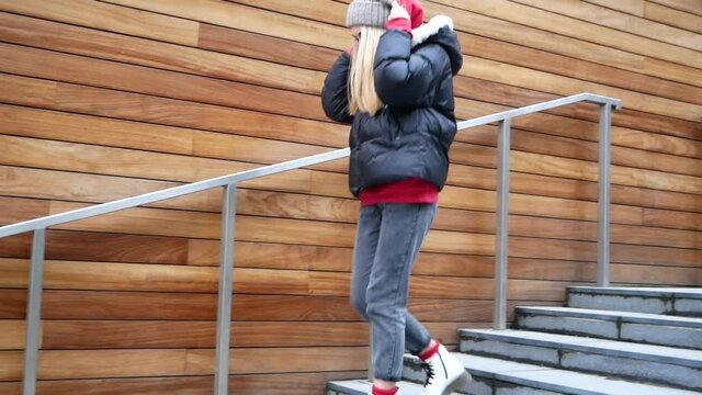 Woman in warm coat walking dow stairs in the street. Slow motion. Lifestyle concept. Young girl in European city, winter or autumn time.