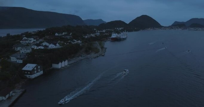 Turning aerial footage that shows Hessa at the biggest bonfire event on Earth and the small boats gathering around it near Alesund, Norway at dusk.