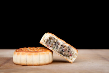A complete mooncake and a broken mooncake on the cutting board in front of a black background
