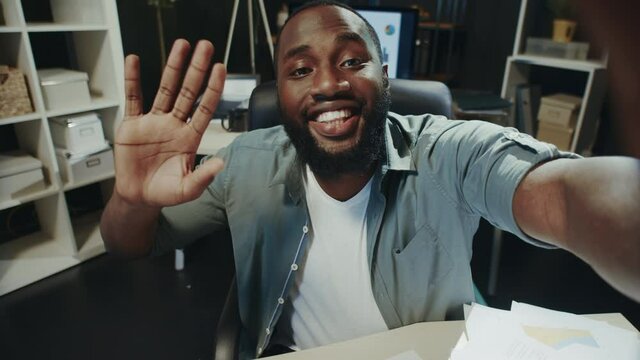 Portrait of smiling afro man saying hi to camera at hipster workplace.