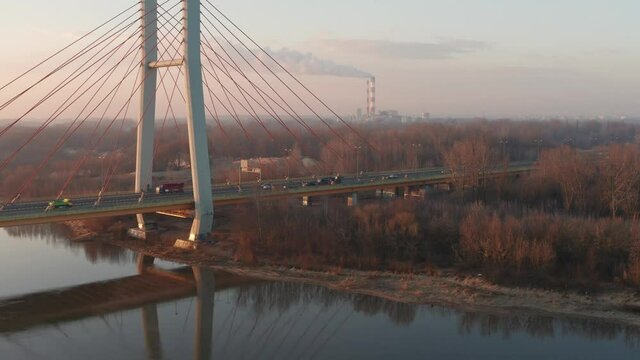 Drone footage of sunrise over bridge full of cars with heat and power plant in the background. Scene takes place in Warsaw, Poland.