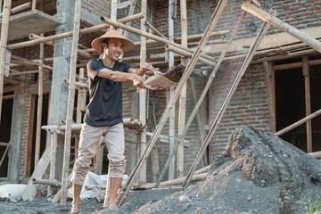 Naklejka na ściany i meble mason holding shovel while carrying sand to sieve against the backdrop of house building