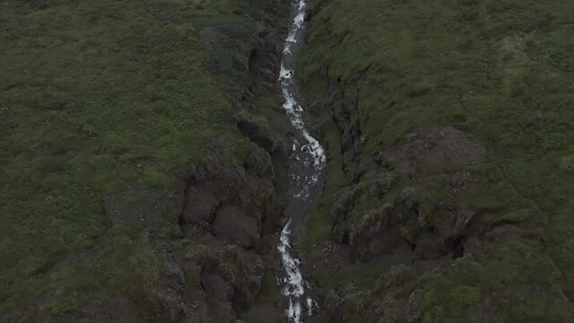 Aerial above run off water from waterfall surrounded by grass field