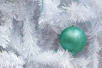 Light cold Christmas background. Branches of a white artificial Christmas tree and a turquoise Christmas ball.