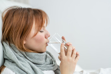 Sick girl sitting on a bed and drinking water from a glass at home