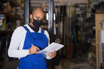 Focused Hispanic salesman wearing protective mask to prevent respiratory infections checking goods availability on shelves of building materials hypermarket