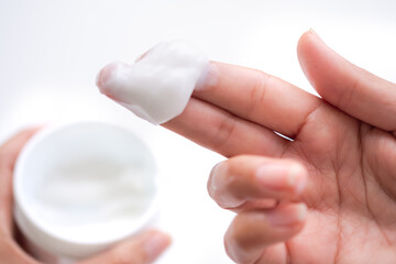 Close up Moisturizing cream  lotion on fingers with blur image of lotion in a jar on white background. for applying or cosmetic allergy test. beauty and healthcare concept. authentic skin tan fingers